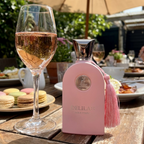 Frasco do perfume Delilah da Maison Alhambra sobre mesa de madeira em ambiente externo.