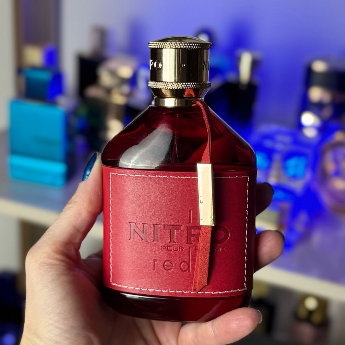 Perfume Dumont Nitro Red segurado em ambiente interno com iluminação azul