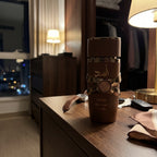 Perfume Lattafa Asad Bourbon sobre móvel de madeira em quarto de hotel com iluminação noturna.