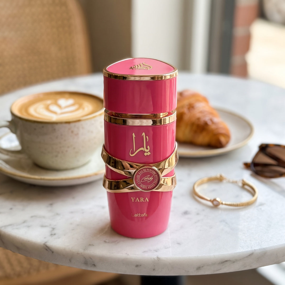 Perfume Lattafa Yara Candy sobre mesa de café com bebida e croissant ao fundo