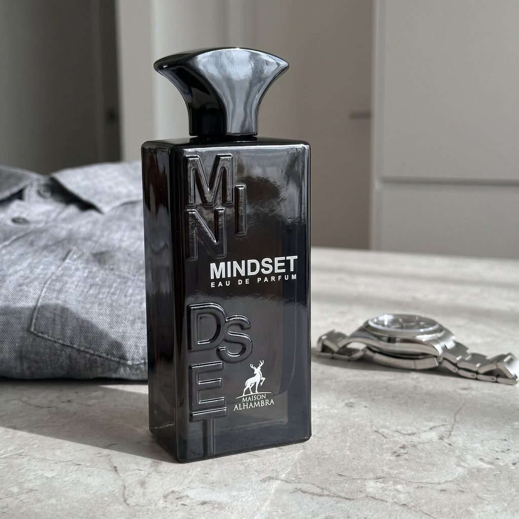Perfume Maison Alhambra Mindset sobre bancada ao lado de camisa social e relógio